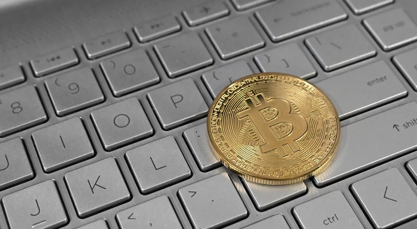 A gold Bitcoin coin resting on a silver laptop keyboard